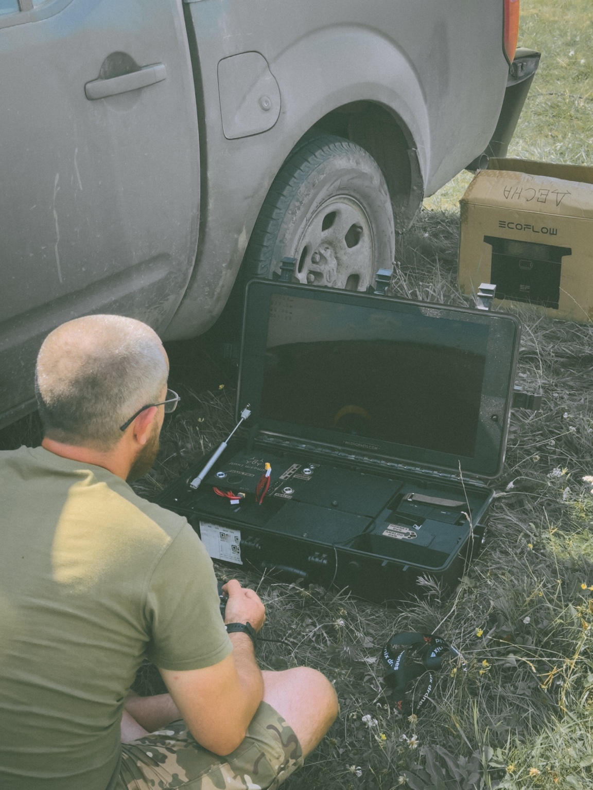 Operator seated in a field beside a vehicle, working at a ruggedised case-mounted control station